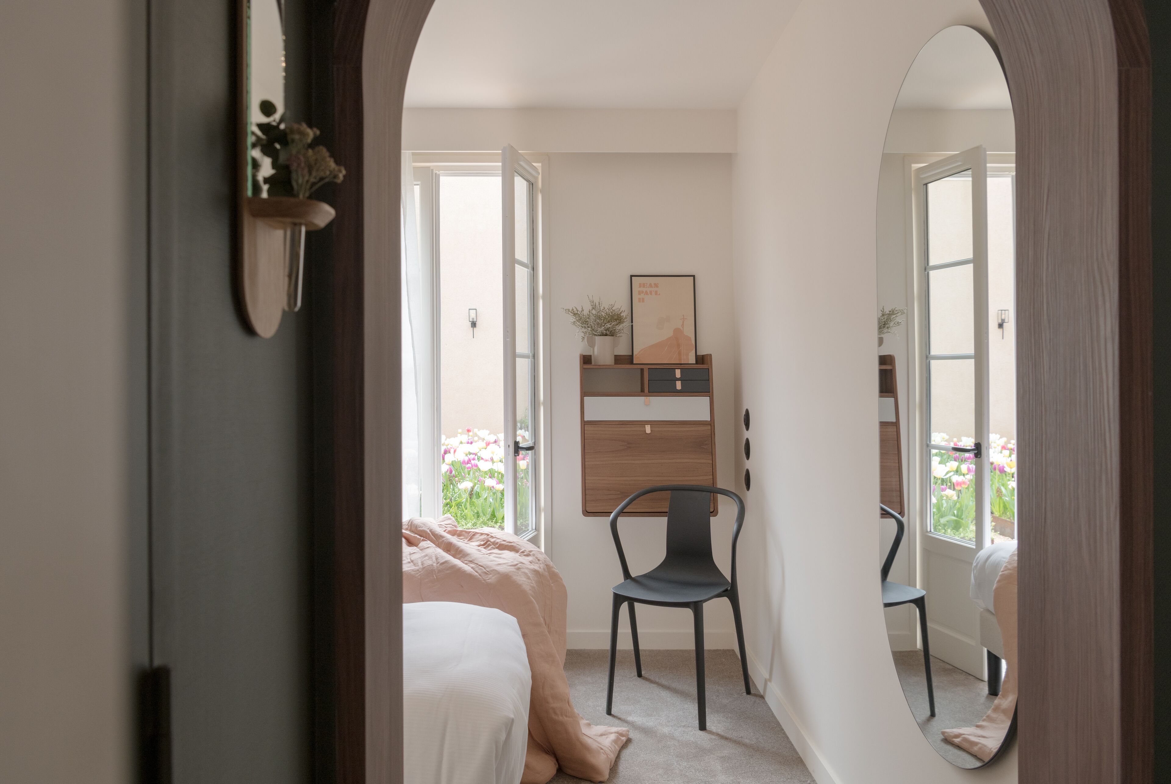 A bedroom with a bed, a chair, a desk, and a window with flowers.