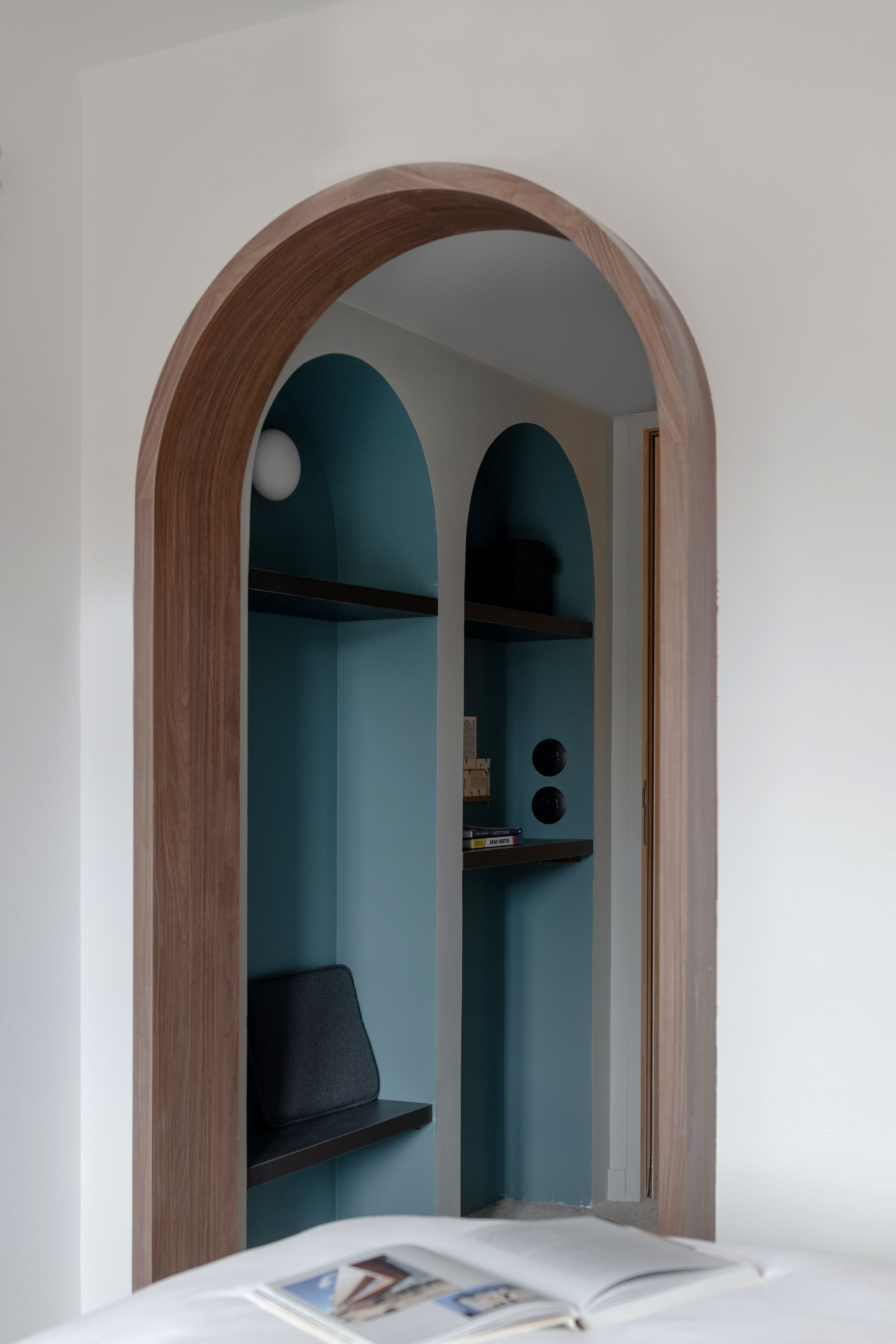 A room with a wooden arched doorway leading to a blue alcove with shelves and a black chair.