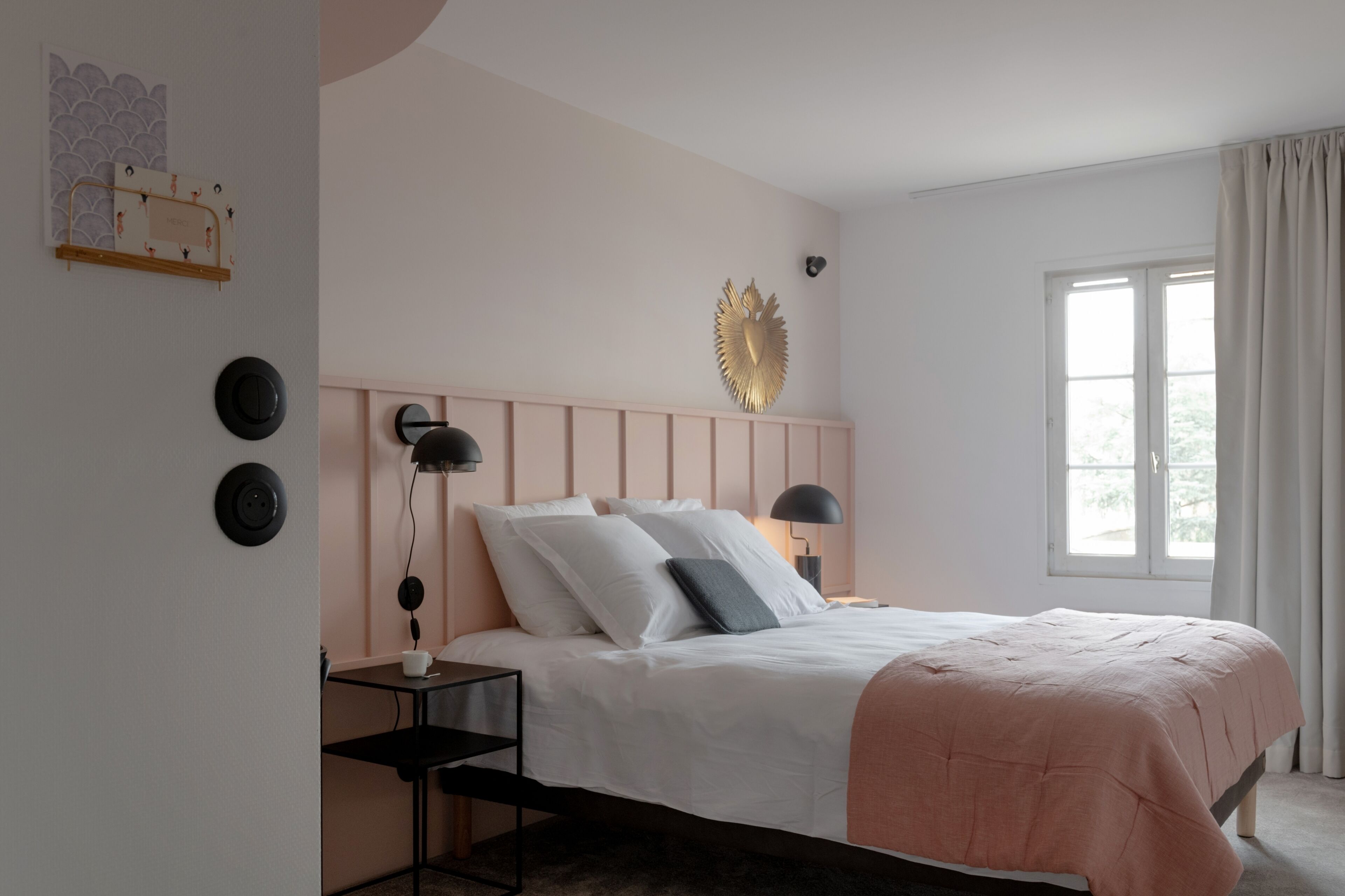 Ein Schlafzimmer mit Bett, Nachttischen, einer Wandleuchte und einem Fenster mit Vorhängen.