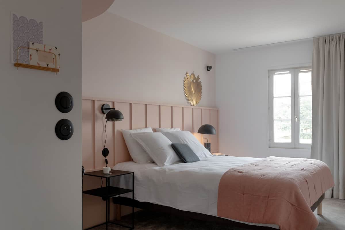 A bedroom with a bed, bedside tables, a wall-mounted light fixture, and a window with curtains.