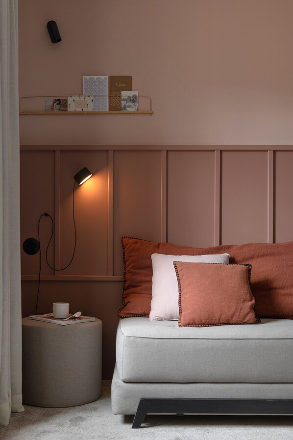 Una habitación acogedora con un sofá, almohadas, una mesita auxiliar, una lámpara y una estantería con objetos decorativos.