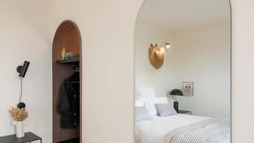 Ein modernes Schlafzimmer mit einem großen Spiegel, einem Bett mit gestreifter Bettwäsche, einem Schreibtisch mit Lampe und einem Kleiderständer.
