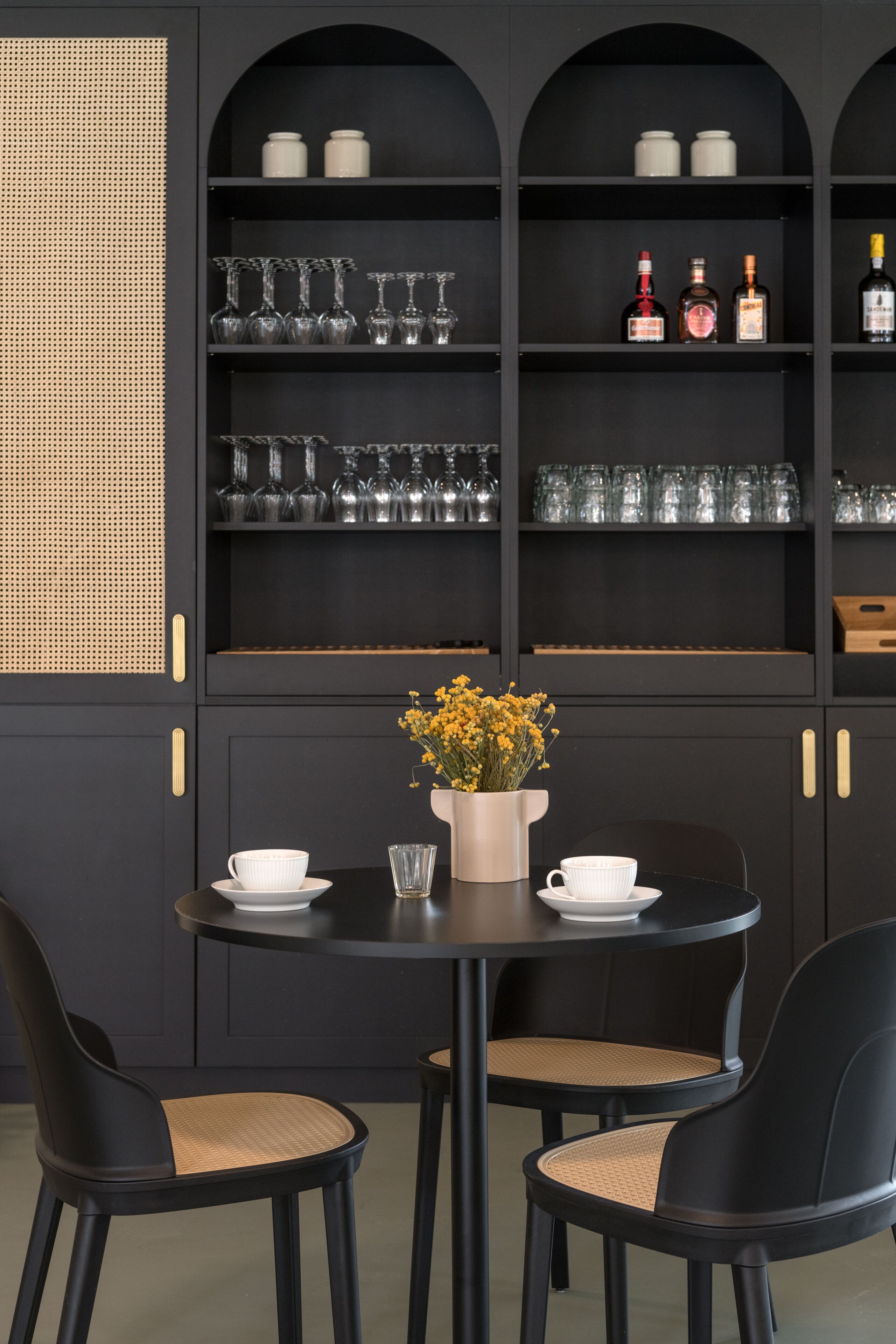 A black dining area with two chairs, a table, and a shelf with glassware and bottles.