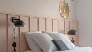 Ein ordentlich bezogenes Bett mit weißen Leinen und zwei Kissen, ein Nachttisch mit Lampe und ein dekoratives Wandbild darüber.