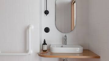 Een badkamer met witte betegelde wanden, een houten wastafelmeubel, een witte wasbak, een spiegel en een toilet.