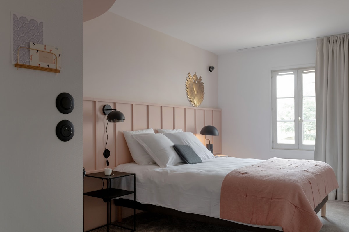 A bedroom with a bed, bedside tables, a wall-mounted light fixture, and a window with curtains.