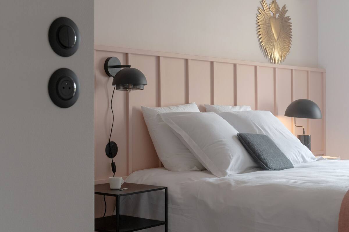 A bedroom with a bed, bedside tables, a wall-mounted light, and a decorative wall piece.