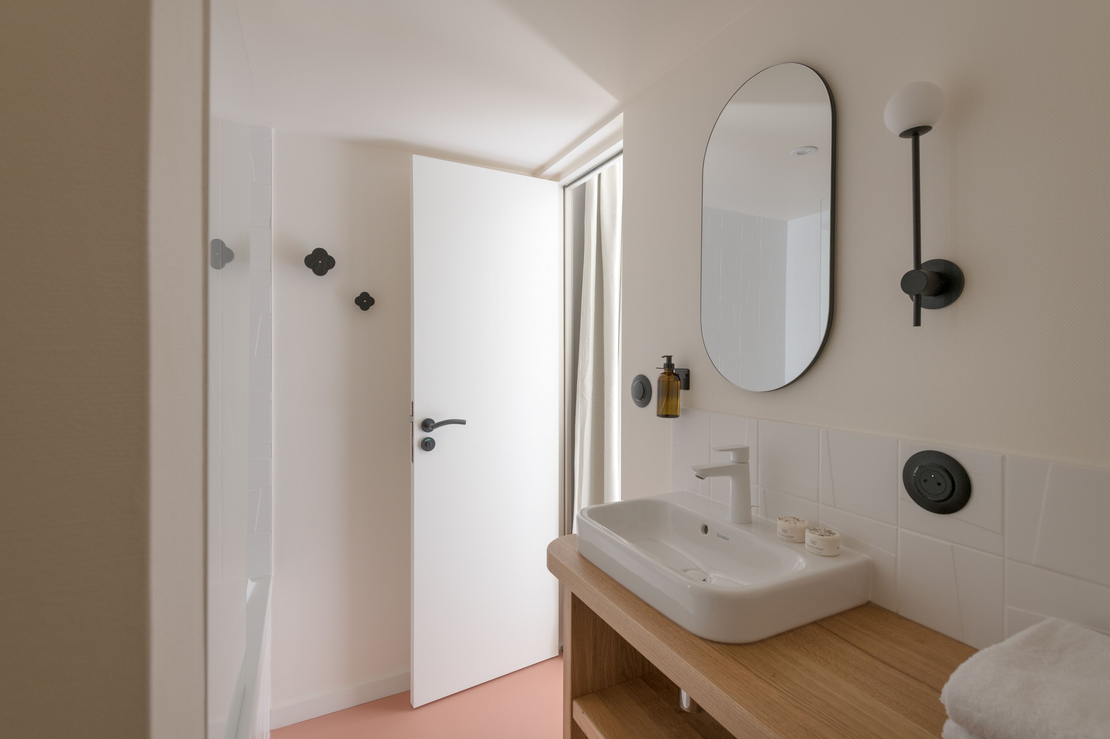 Une salle de bain moderne avec un lavabo blanc, un miroir et une porte donnant sur une autre pièce.