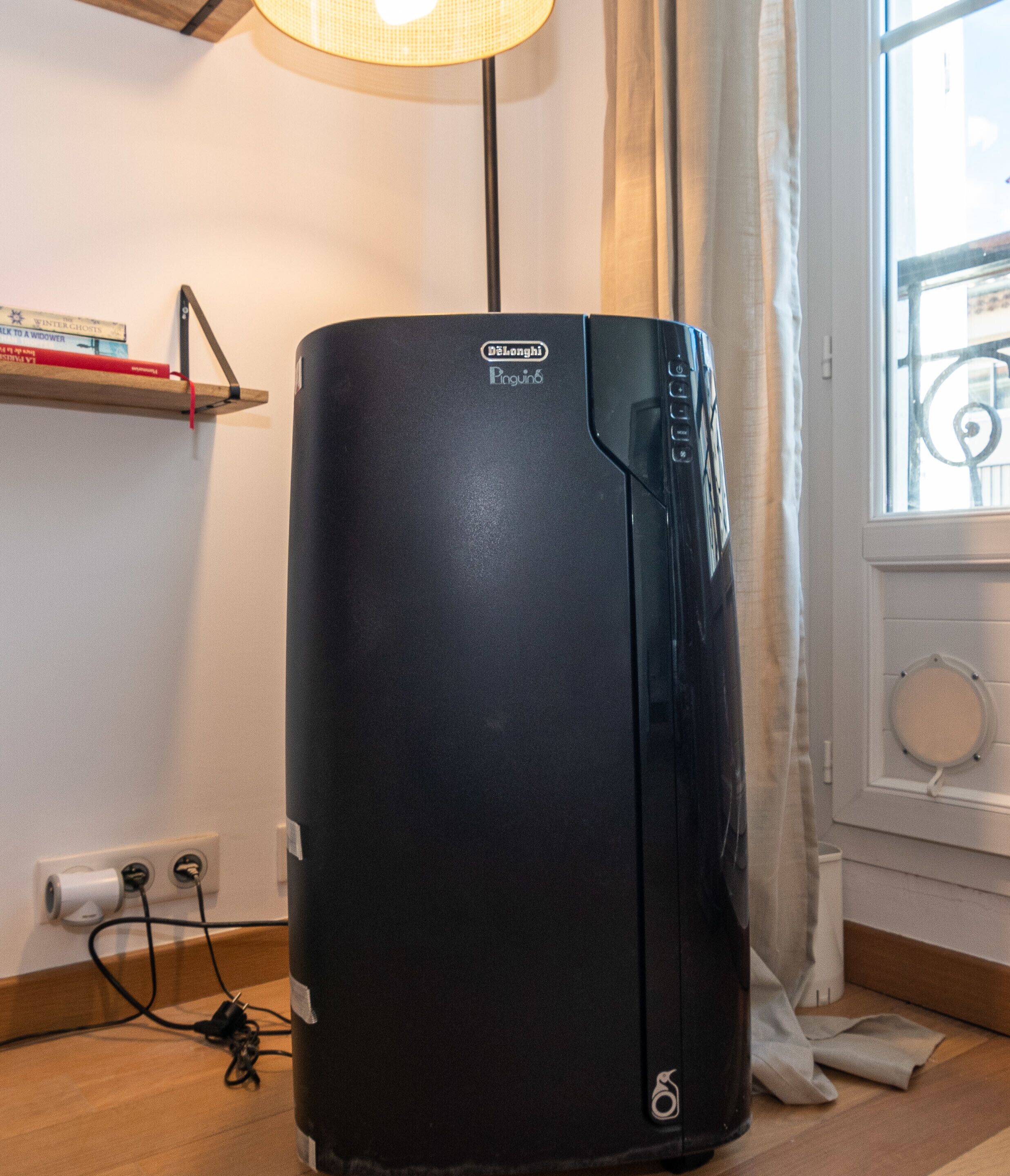 Et sort køleskab med Delonghi logo, et strømkabel og en rude med gardin.
