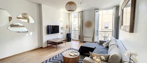 Una sala de estar moderna con sofá, mesa de centro, televisor y espejos decorativos.
