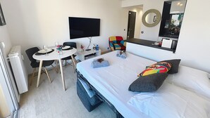 A hotel room with a bed, a desk with a chair, a television, a mirror, and a small table with a vase and flowers.
