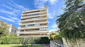 A multi-story residential building with balconies, surrounded by greenery and a clear sky.