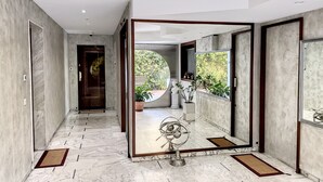 A hallway with marble flooring, a large mirror reflecting a statue and greenery, and a door leading to another room.