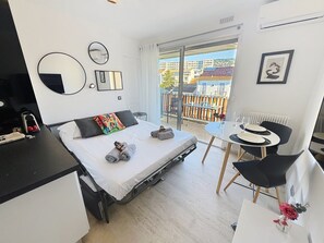 Une chambre d’hôtel moderne comprenant un lit, une petite table avec des chaises, un balcon donnant sur des immeubles et un radiateur.
