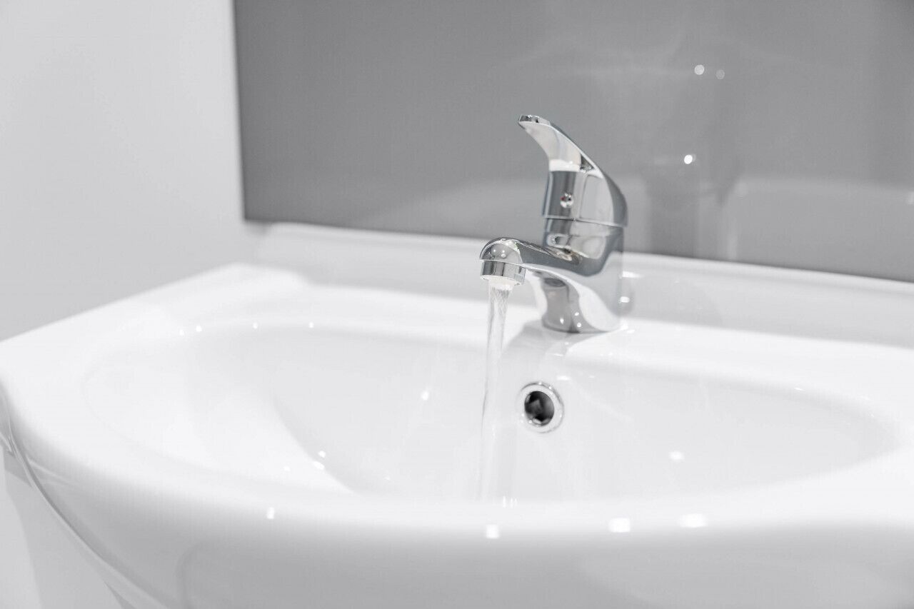 Ein weißes Waschbecken mit chromfarbenem Wasserhahn und einem Spiegel darüber.
