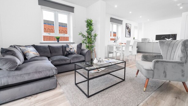 A modern living room with a grey sofa, a glass coffee table, and a grey armchair. - The Marsons Collection - 2 Bed Apartment- Parking (Birmingham)