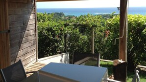 A covered outdoor seating area with a table and chairs, overlooking a lush garden and the ocean. - Baobab 3 Vacation Rental – Tropical Charm & Ocean-View Pool (Sainte-Anne)