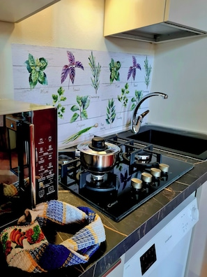 Cozinha com fogão a gás, micro-ondas e forno embutido. Há uma pia com torneira e um colcha colorida no balcão.