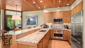 A modern kitchen with wooden cabinets, granite countertops, stainless steel appliances, and a large island with seating.