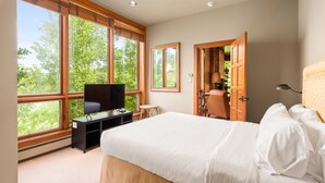 A bedroom with a large bed, a television, and a window with a view of trees.