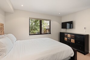 Een slaapkamer met een bed, een raam, een dressoir en een televisie.