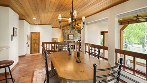 A spacious dining area with a wooden table and chairs, a chandelier, and a view of the outdoors through large windows. - Sweeping down-valley views and comfortable upgrades. (Snowmass Village)