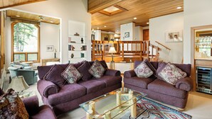 A spacious living room with two purple sofas, a glass coffee table, and a wooden staircase leading to an upper level. - Sweeping down-valley views and comfortable upgrades. (Snowmass Village)