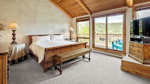 Un dormitorio con cama de madera, banco y cómoda, ventanas amplias con vistas a un espacio de estar exterior.