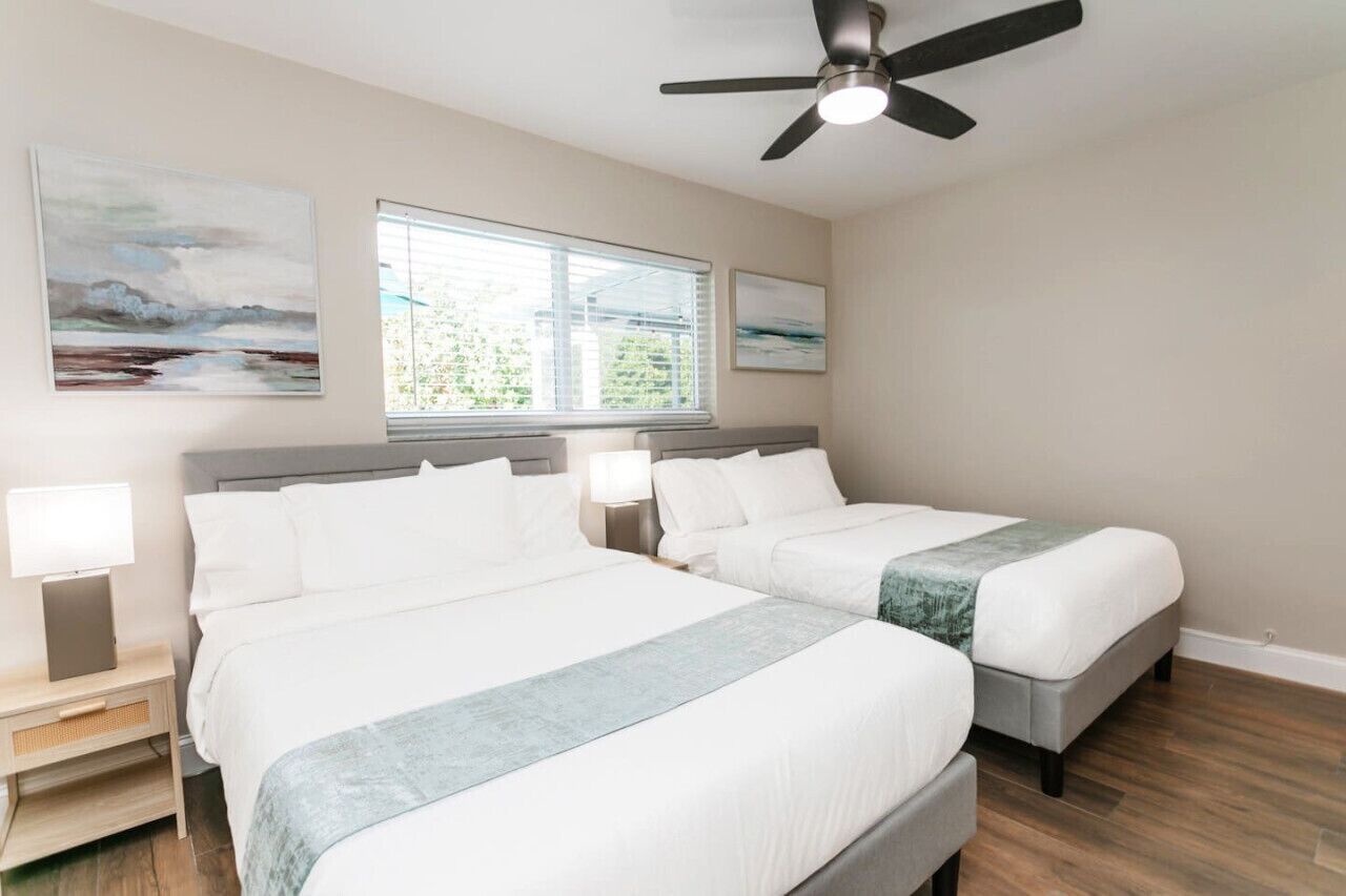 A hotel room with two beds, a ceiling fan, and artwork on the walls.