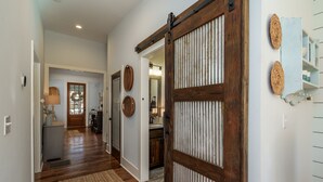 Un corridoio con una porta in legno, un cesto di vimini appeso al muro e una zona cucina visibile attraverso una porta aperta.