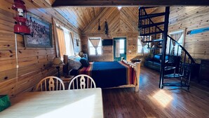 L’intérieur chaleureux d’un chalet, avec un revêtement mural en bois, un lit, une table à manger et un escalier.