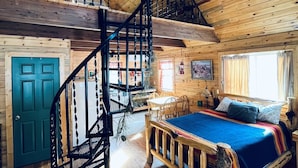 L’intérieur d’un chalet en bois est doté d’un escalier en colimaçon, d’un lit recouvert d’une couverture bleue, de planchers en bois et d’un coin repas.