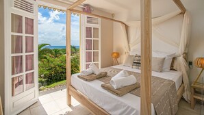 Uma cama com dossel e cortina, vista para o oceano e um jardim tropical lá fora.