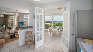 Cozinha moderna com área de refeições, portas abertas para uma varanda com vista para o oceano.
