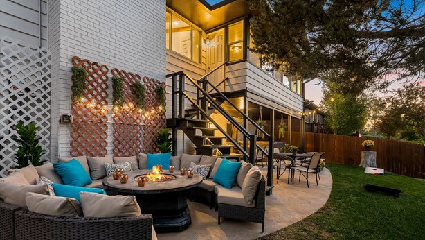 A modern outdoor patio with a fire pit, wicker furniture, and a staircase leading to an upper level.