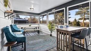 A modern interior with a dining area, blue chairs, a wooden table, and large windows offering a view of trees and mountains.