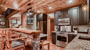 A rustic kitchen with wooden beams, a stone island, bar stools, a stainless steel refrigerator, a microwave, and an oven. - Book 3+4th FREE Amazing views, Hot Tub, Pool Table, Hot Springs, Moose sightings (Fairplay)