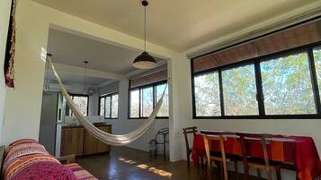 A spacious living area with a hammock, a dining table with chairs, and large windows.