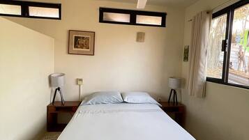 A bedroom with a single bed, a ceiling fan, two bedside tables with lamps, a framed picture on the wall, and a window with curtains.
