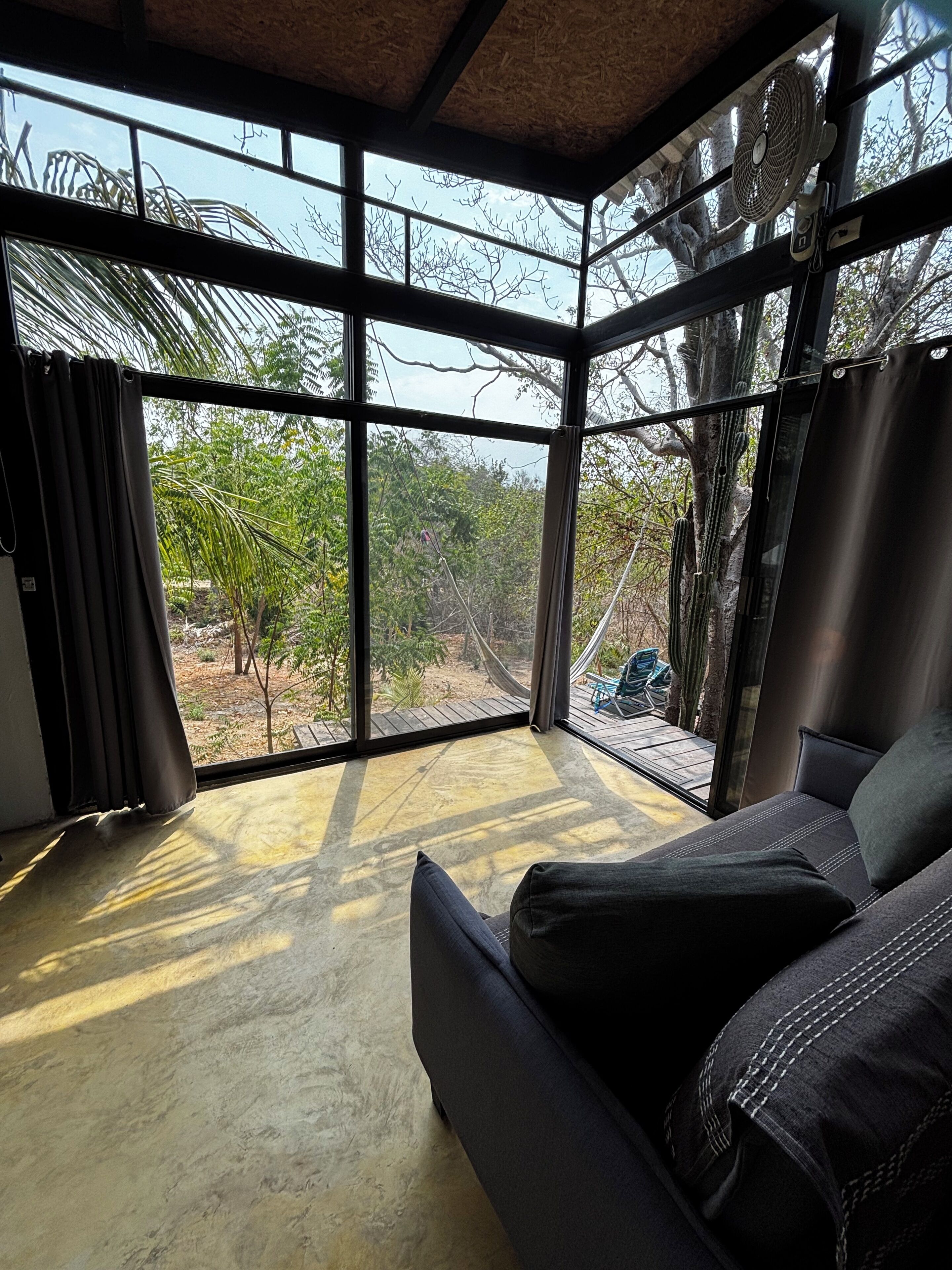A room with a large window, a ceiling fan, and a sofa.