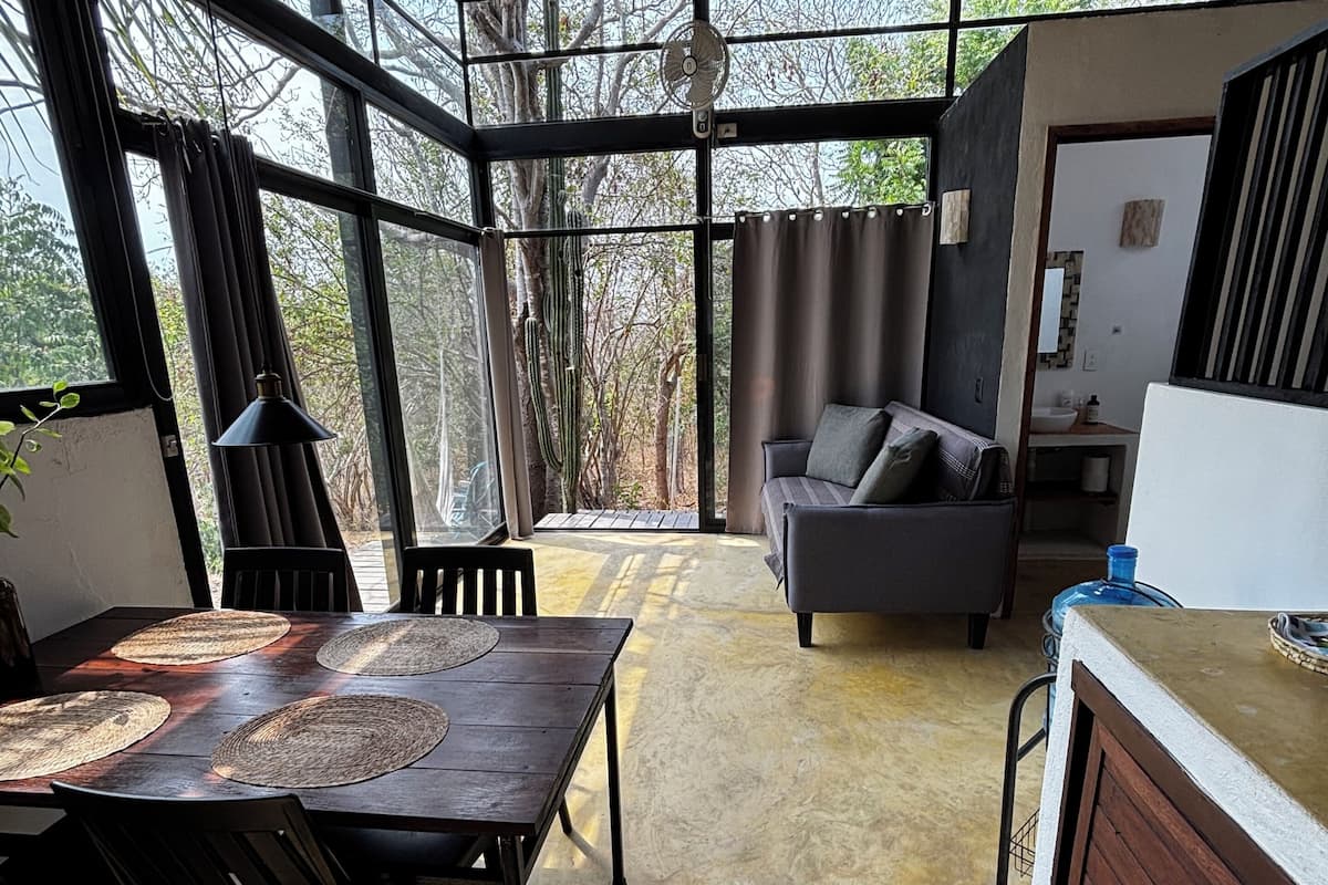 Une pièce spacieuse comprenant une table à manger, des chaises, un canapé et une grande fenêtre donnant sur la forêt.