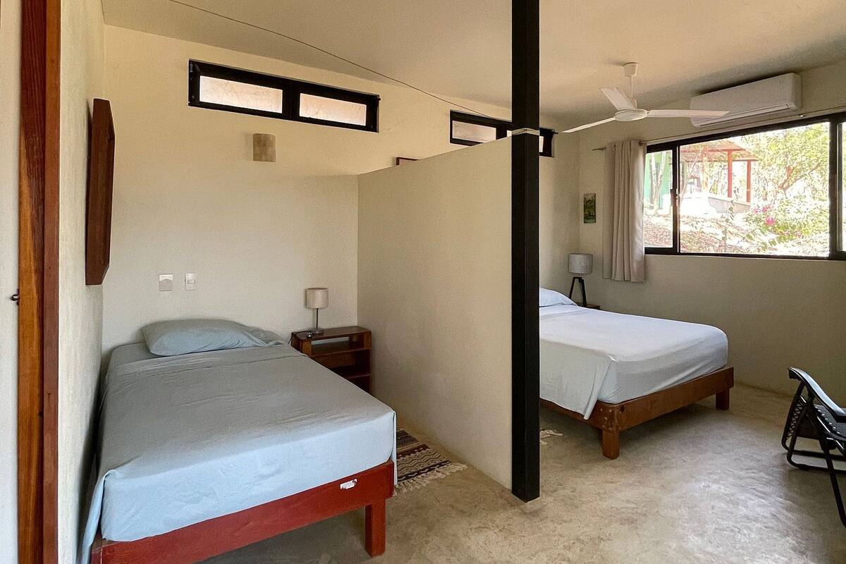Une chambre avec deux lits, un ventilateur de plafond et une fenêtre avec des rideaux.