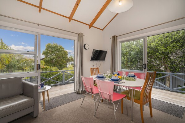 A dining area with a table set for four, surrounded by pink chairs, a grey sofa, and a small side table.