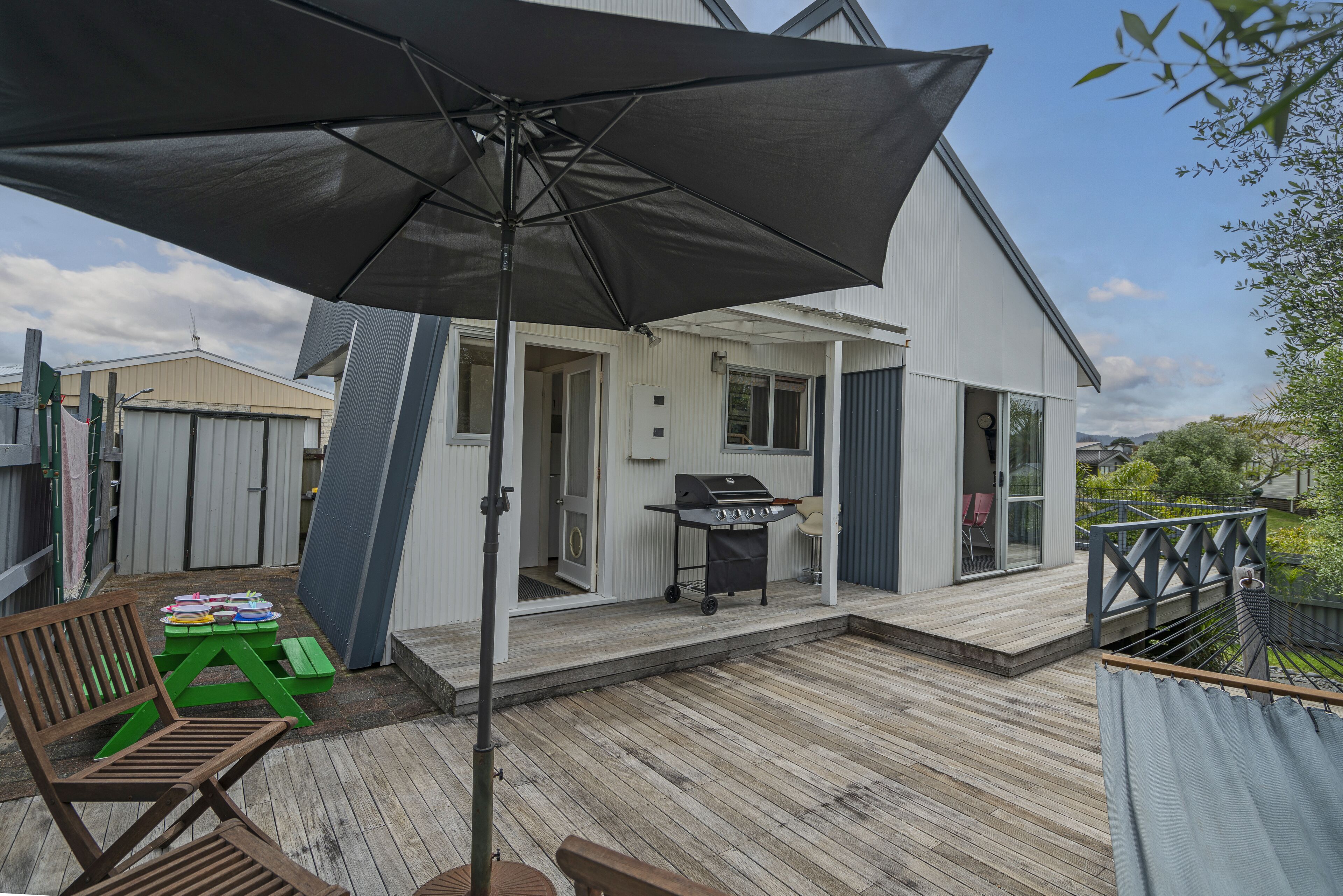 A wooden deck with a grill, a green table, and a bench.