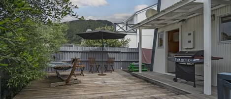 Una terraza de madera con mobiliario exterior, una parrilla y un área cubierta con sillas.