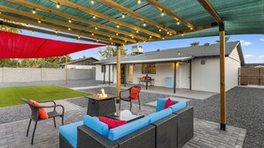 Eine Terrasse im Freien mit Korbmöbeln, einem Feuerkorb und Lichterketten.
