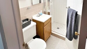 Et badeværelse med toilet, vask, spejl, brusebad og et håndklædestativ.