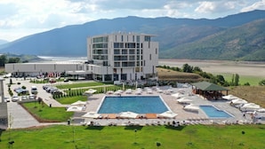 A modern hotel with a pool area, surrounded by mountains and a parking lot. - Lakeside Hotel (Prizren)