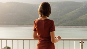 A person standing on a balcony overlooking a body of water with hills in the background. - Lakeside Hotel (Prizren)