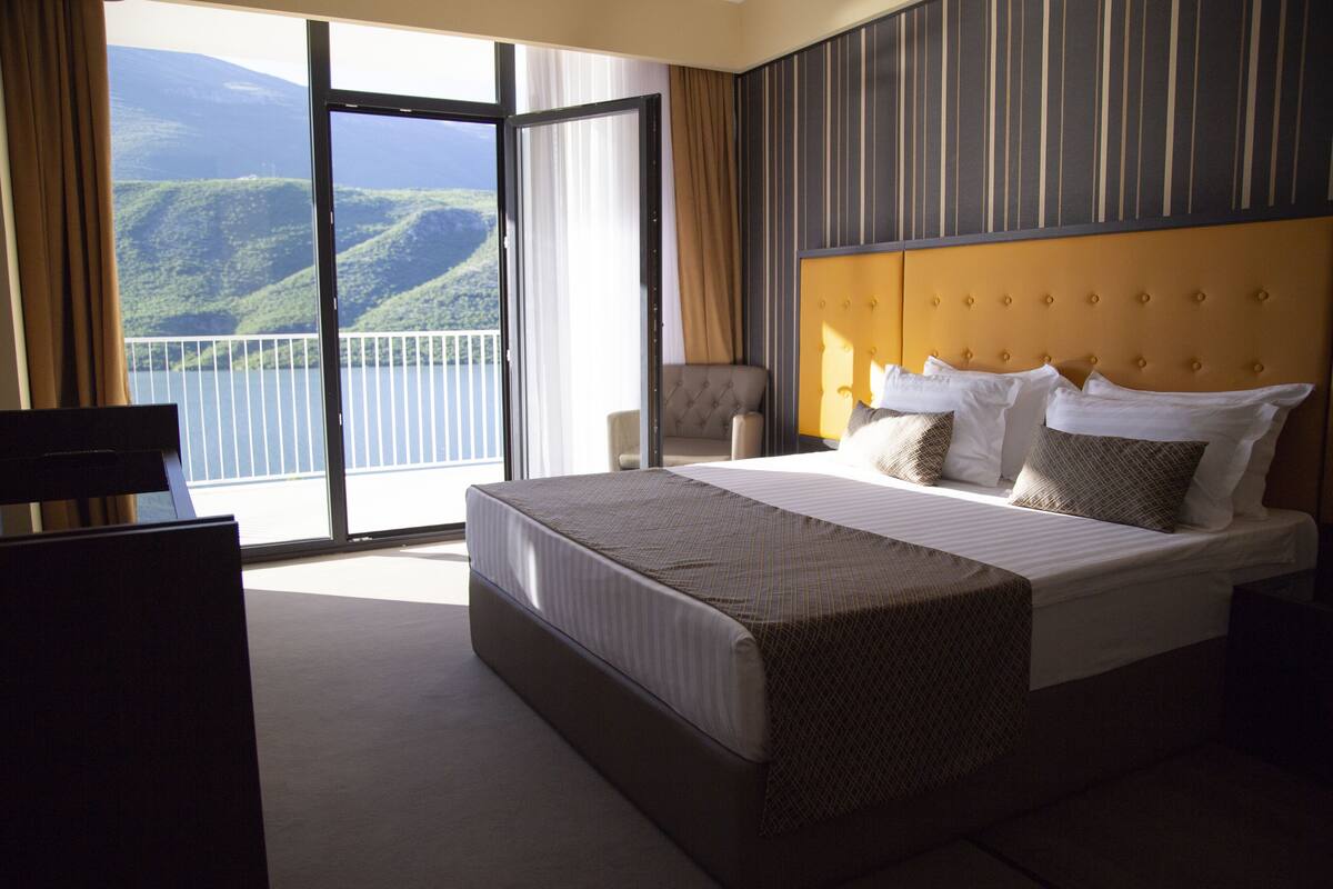 A hotel room with a large bed, a view of the mountains, and a balcony.
